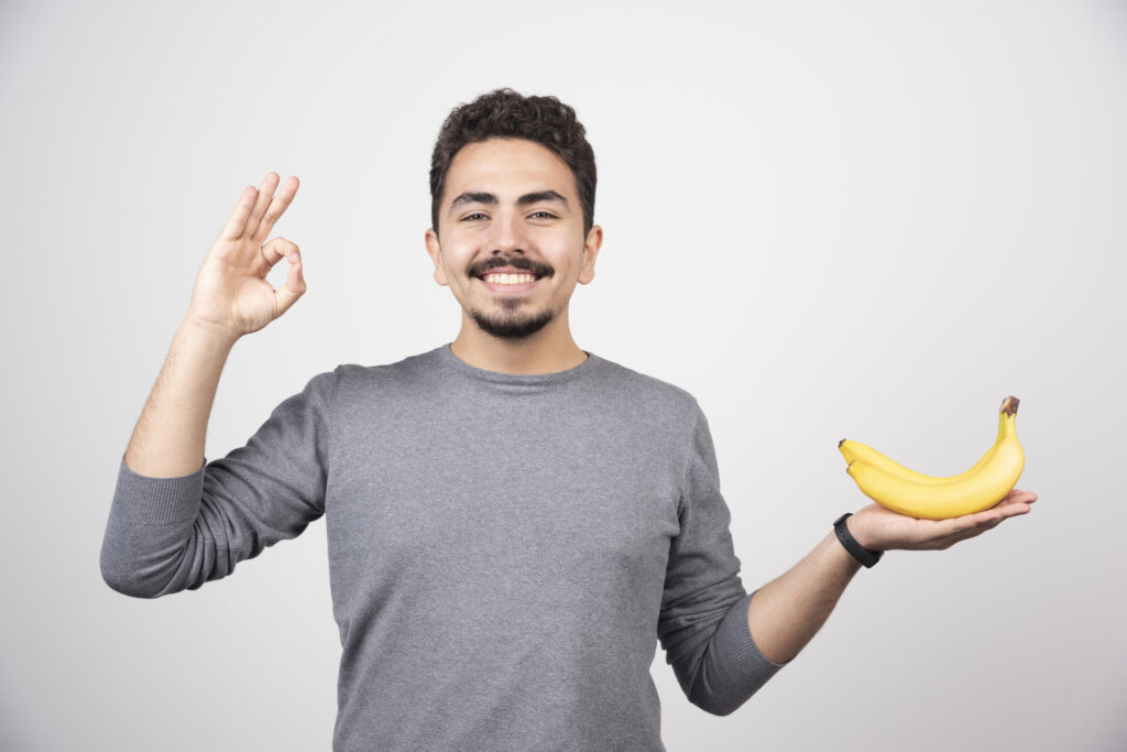 brunette male holding banana giving ok sign